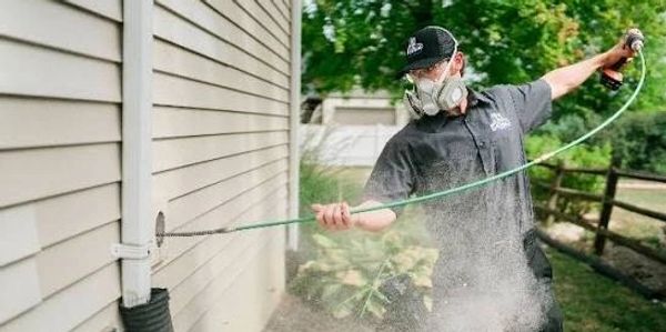 Technician using equipment to spray and clean house siding outdoors.