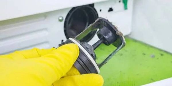 Hand in yellow glove holding a dirty washing machine filter.