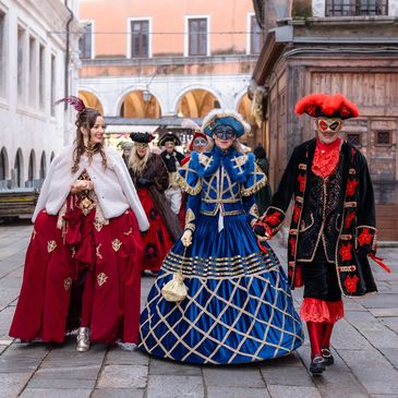 People dressed in elaborate Venetian carnival costumes walking outdoors.