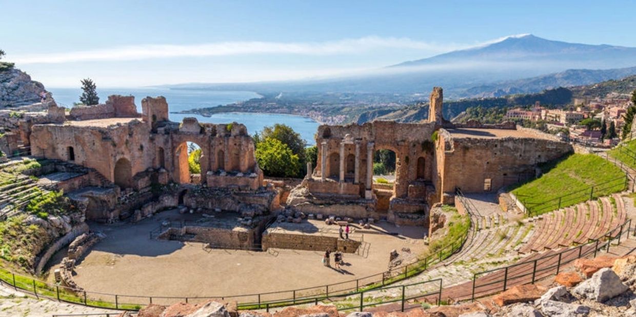 Ancient amphitheater ruins with a coastal view and distant mountain.