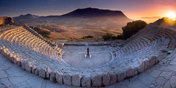 Ancient stone amphitheater at sunset with mountainous backdrop.