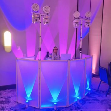 Person behind a blue-lit DJ booth with lighting equipment.