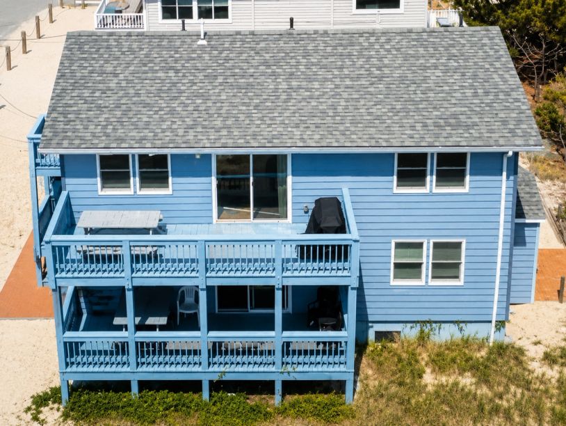 Blue beach house with two balconies and sandy surroundings.