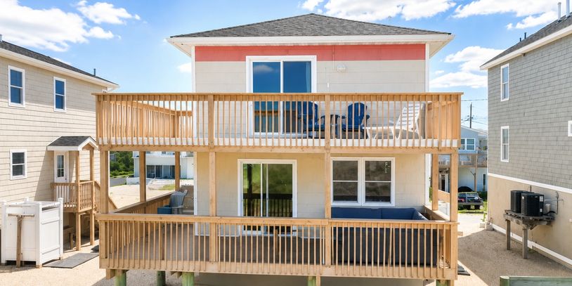Two-story beach house with wooden decks and outdoor seating.