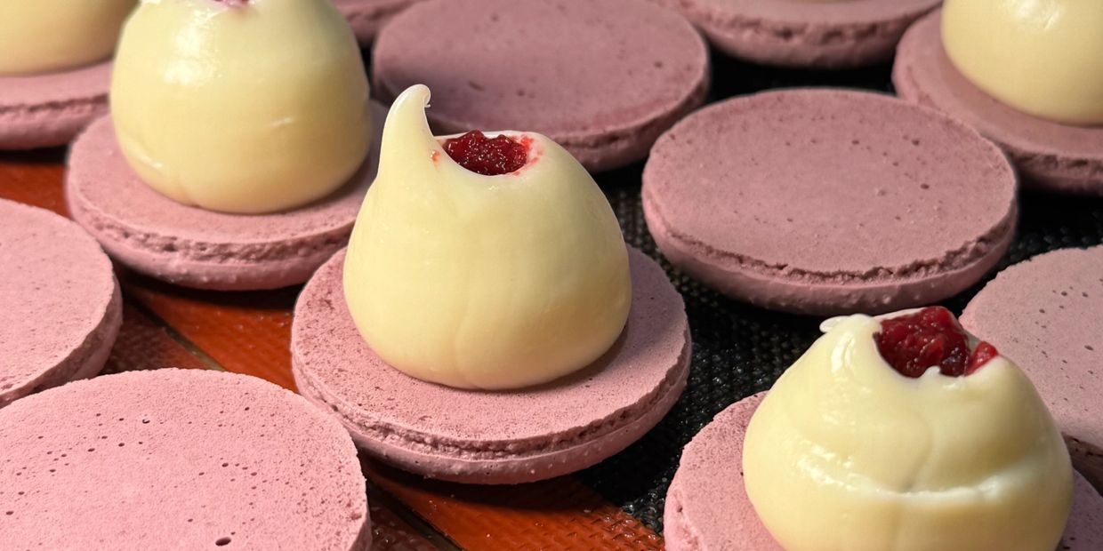 Pink macaron shells with white chocolate and raspberry filling being assembled.