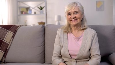 Smiling woman sitting on couch at home, symbolizing hope, and healing through grief counseling.