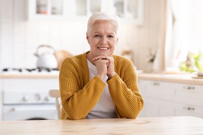 Smiling older woman sitting at home, showing peace, resilience, and recovery through trauma therapy.