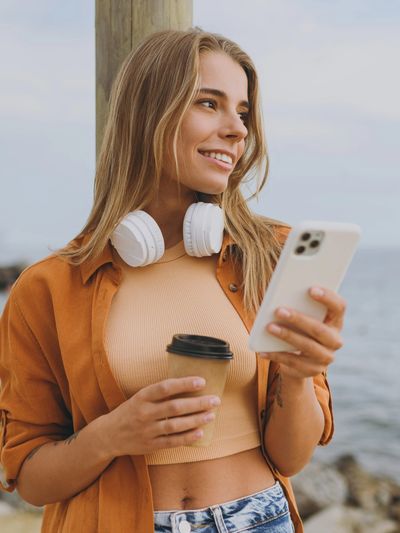 Woman on Florida beach with phone and coffee, symbolizing calm support and virtual anxiety therapy.