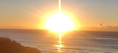 Bright sunrise over calm ocean waters with silhouetted land.