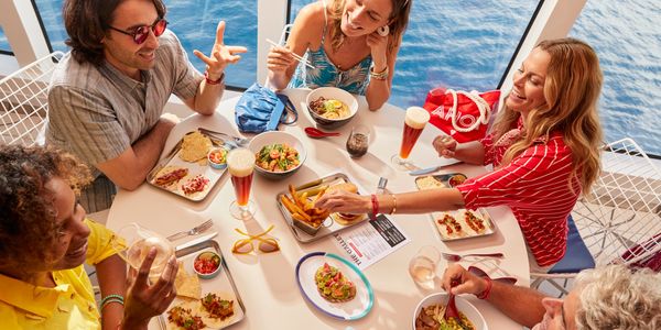 Group of friends enjoying a meal and drinks by the ocean on a sunny day.