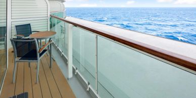 A cozy balcony on a ship with a table and chairs overlooking the ocean.