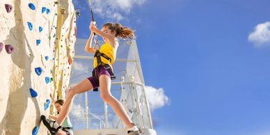 Two girls climbing an outdoor rock wall on a sunny day.