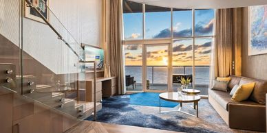 Modern living room with ocean view and sunset through large windows.