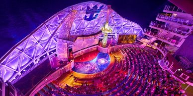A vibrant nighttime view of a cruise ship's outdoor theater with a pool and audience seating.