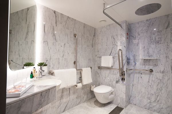 Modern accessible bathroom with marble walls and safety rails.