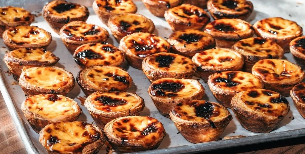 Tray filled with freshly baked Portuguese egg tarts with caramelized tops.