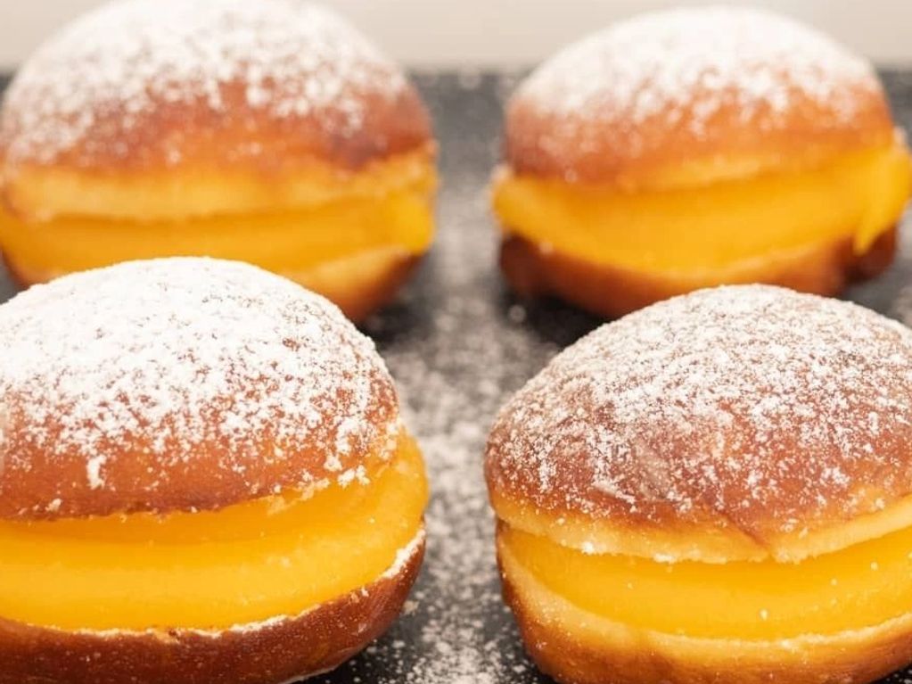 Four custard-filled buns dusted with powdered sugar on a dark surface.