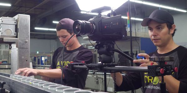 Two men filming a production line with a professional camera and lighting setup.