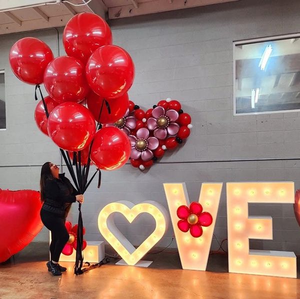 Woman holding large red balloons next to illuminated LOVE sign.