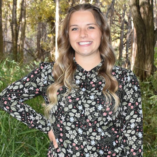 Smiling woman with long hair in floral dress outdoors.
