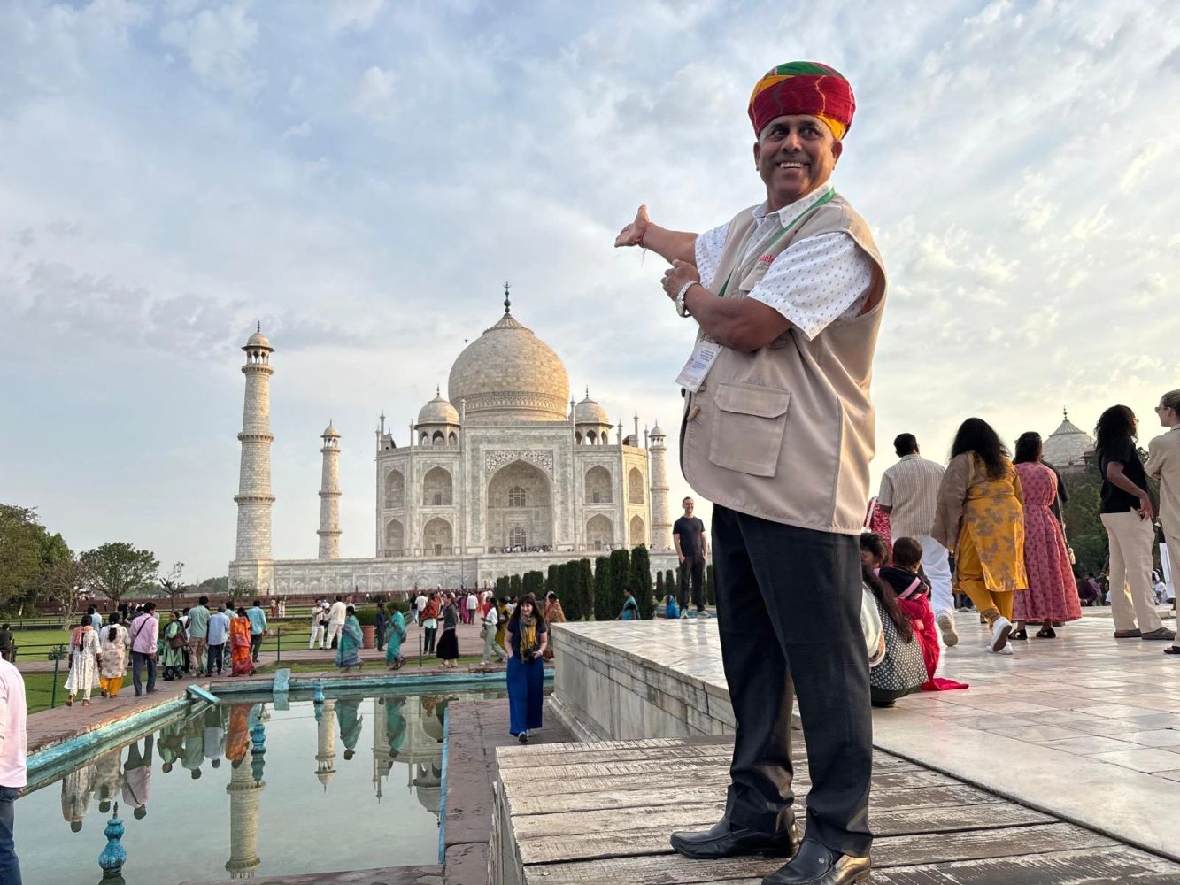 Bahadur Singh steht mit lächelnder, begrüßender Geste vor dem majestätischen Taj Mahal in Agra.