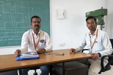 Two men sitting at a desk in a classroom or office setting.