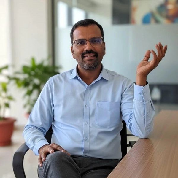 A man in glasses and light blue shirt smiling while sitting at a desk.