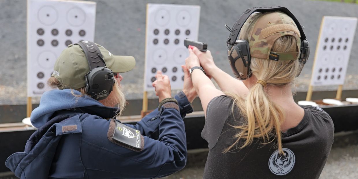 Two women at a shooting range aiming pistols at targets.