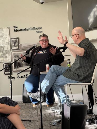 Two individuals engaged in a lively discussion with microphones in a casual setting.