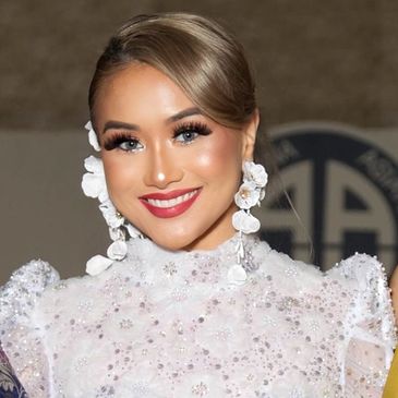 A smiling woman with elegant makeup and floral earrings in a white embellished dress.