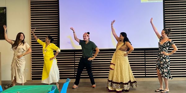 Five women posing with raised arms in a dance pose indoors.