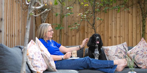 Woman relaxing with her dog on a cozy outdoor sofa under a wooden pergola.