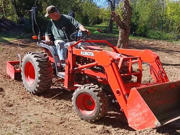 Man operating an orange Kubota tractor on a dirt field.