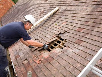 A worker repairs damaged roof tiles on a house.