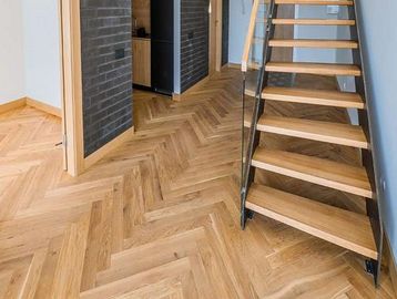 Modern wooden staircase and herringbone wood flooring in a minimalist hallway.