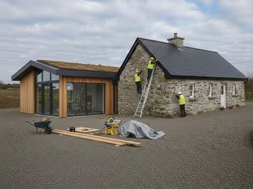 Workers in safety gear renovating a stone house with a modern wooden extension.