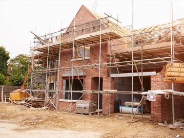 Brick house under construction with scaffolding and building materials.