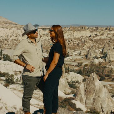 A couple stands smiling amidst rocky desert formations under a clear blue sky.