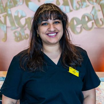 Smiling woman in black scrubs with a name tag at a reception desk.