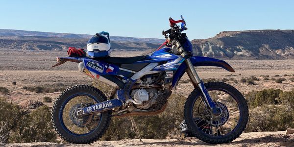 Blue Yamaha dirt bike parked in a desert landscape with a helmet on the seat.