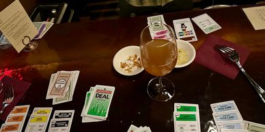 Tabletop game session with Monopoly Deal cards and a drink.