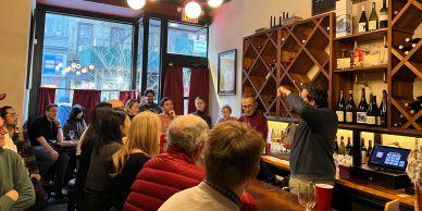 A lively wine tasting event with a presenter and attentive audience in a cozy bar.