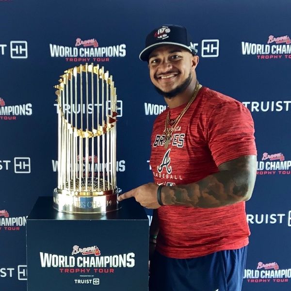Man in Braves gear proudly points at World Series trophy on display.