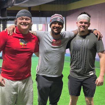 Three friends smiling inside a sports facility with arms around each other.