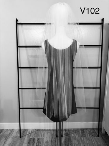 Long white bridal veil displayed on mannequin against black ladder backdrop.