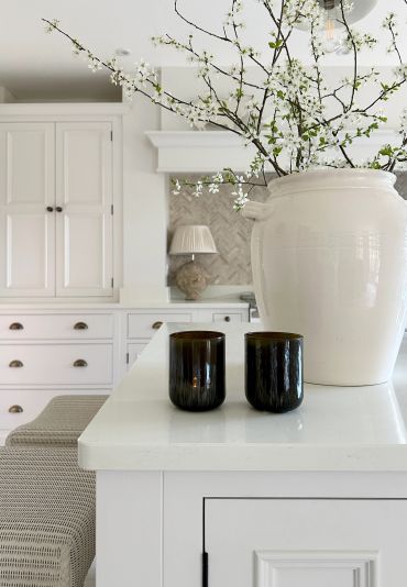 White kitchen island with large vase and two dark glasses.