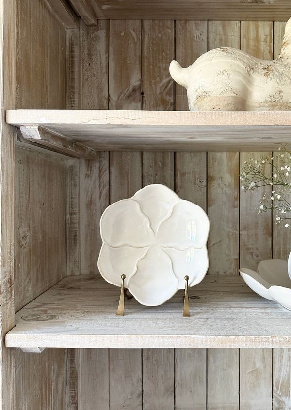 White ceramic flower-shaped plate on a rustic wooden shelf.