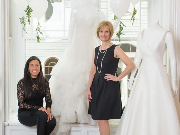 Two women in black dresses posing with white wedding gowns and balloons.