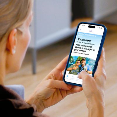 Person holding a phone displaying the Bali Gems app for trusted Bali phone book services.
