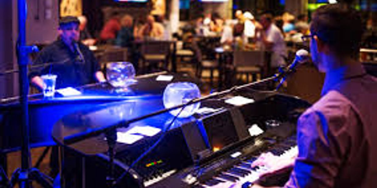 Two musicians playing pianos in a dimly lit restaurant with an audience.